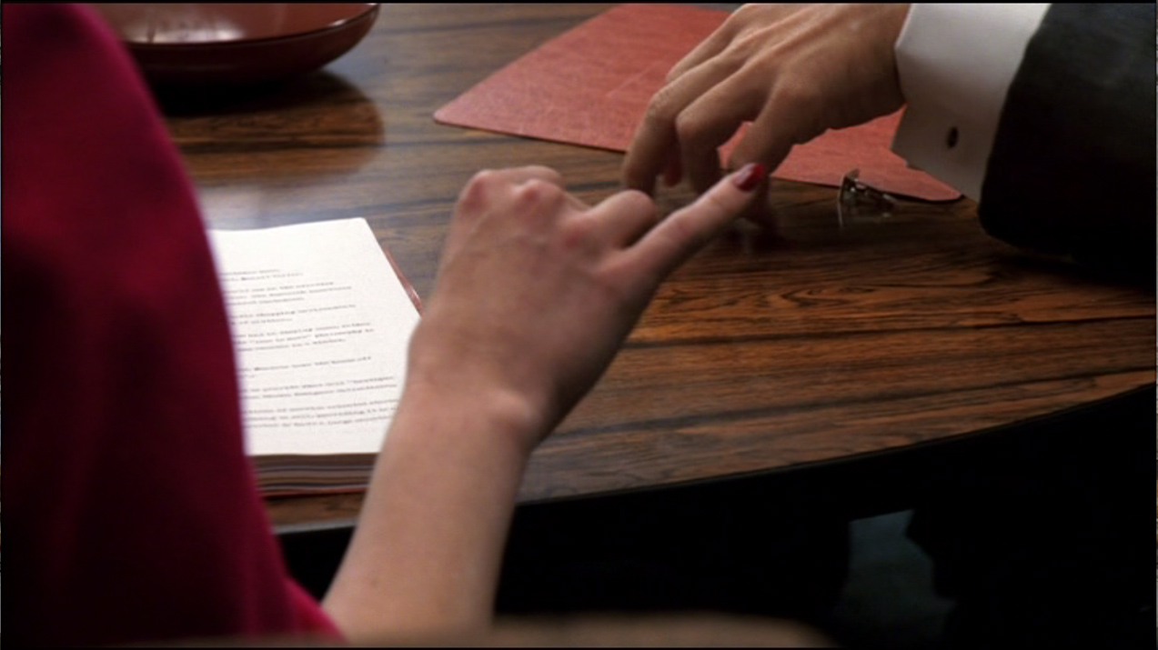 Rachel Menken (Maggie Siff) repousse d’une pichenette le bouton de manchette que Don Draper a laissé tomber sur la table de la salle de conférence
